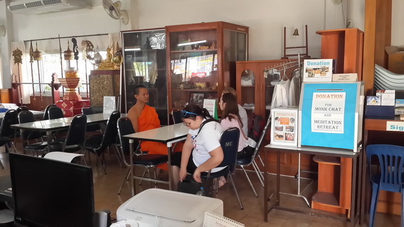 Indoor Donation Area Scene at Wat Suan Dok Indoor scene with women and a monk seated at tables and donation boxes displayed at Wat Suan Dok.