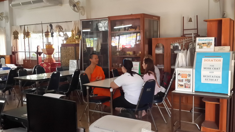 Indoor Meeting Scene at Suan Dok Temple Three individuals seated indoors, with statues and cabinets in the background at Suan Dok Temple.