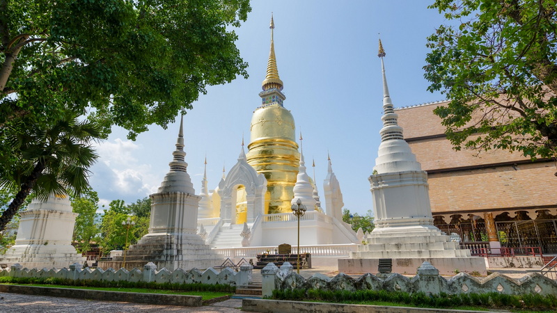 Wat Suan Dok Pagoda at Suan Dok Temple White and gold pagoda with spires under blue sky, surrounded by trees at Suan Dok Temple.