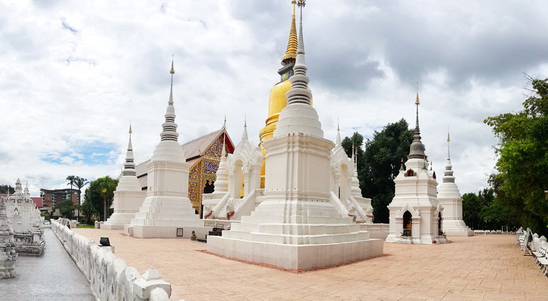 White and gold stupas surrounded by trees in a temple complex at Wat Suan Dok.