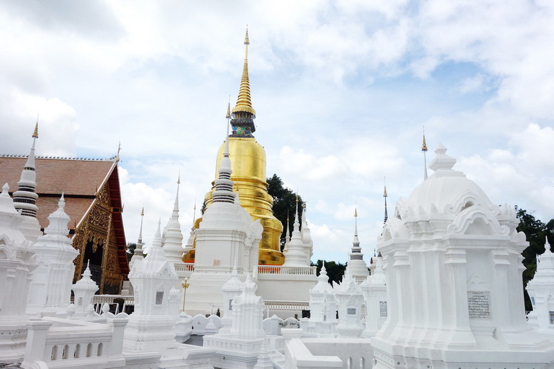 White stupas and a golden pagoda under a partly cloudy sky at a temple complex at Wat Suan Dok.