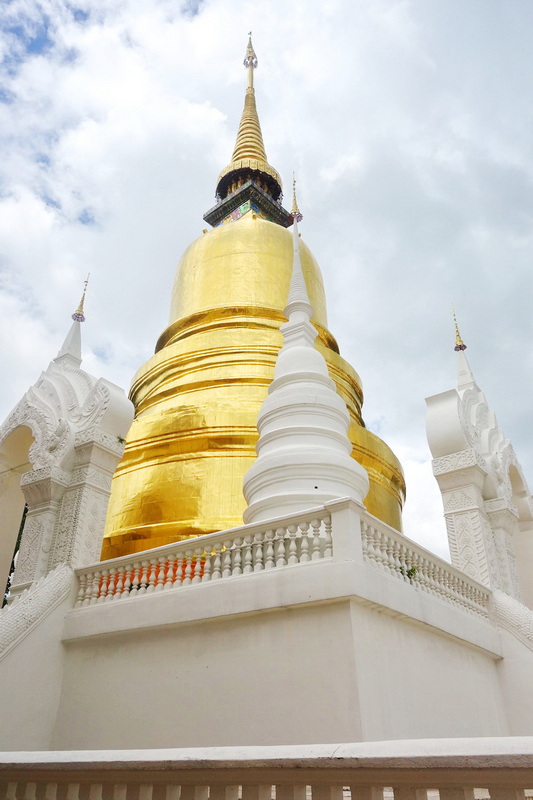 Golden stupa with spire and white architectural details under cloudy sky at Wat Suan Dok.