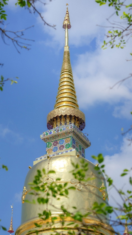 Gold Spire with Mosaic Decorations at Suan Dok Temple Golden spire with mosaic tiles reaching towards the sky, framed by green leaves at Suan Dok Temple.