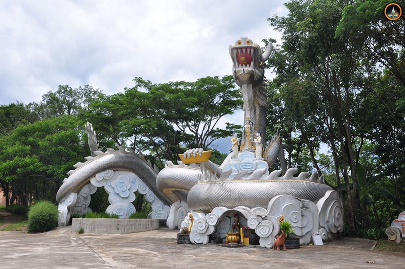 Dragon Sculpture amidst Greenery at Wat Thaton Large silver dragon sculpture with open mouth and detailed features amid lush trees at Wat Thaton.