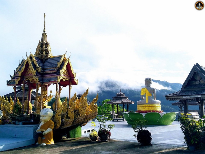 Traditional boat sculpture with golden details and monk statues against mountain scenery at Tha Ton Temple.