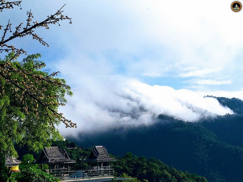 Mountain landscape with clouds, trees, and traditional wooden rooftops at Tha Ton Temple.