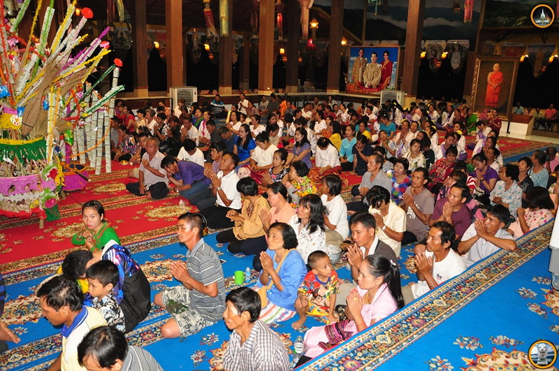 Group of people praying inside a temple with colorful decorations and offerings at Tha Ton Temple.