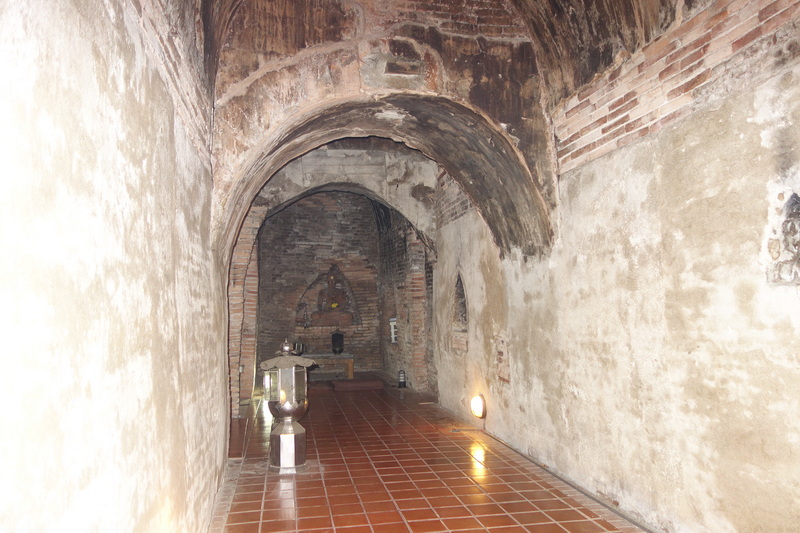 Interior of a brick tunnel with arched ceiling and small shrine at the end at Umong Temple.