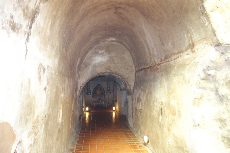 Underground tunnel leading to a small shrine with statues and candles at Umong Temple.