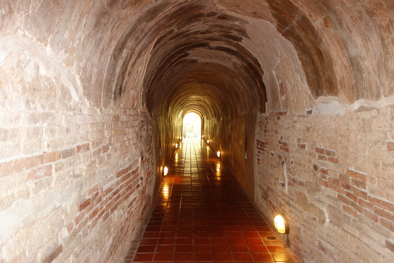 Brick tunnel with arched ceiling and lights leading outside daylight at Wat Umong.