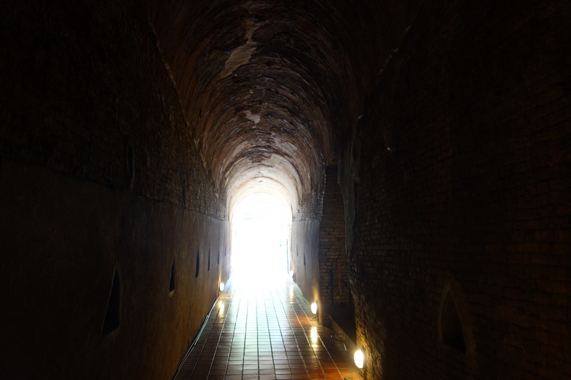 Dark brick tunnel with arched ceiling and light at the end at Umong Temple.