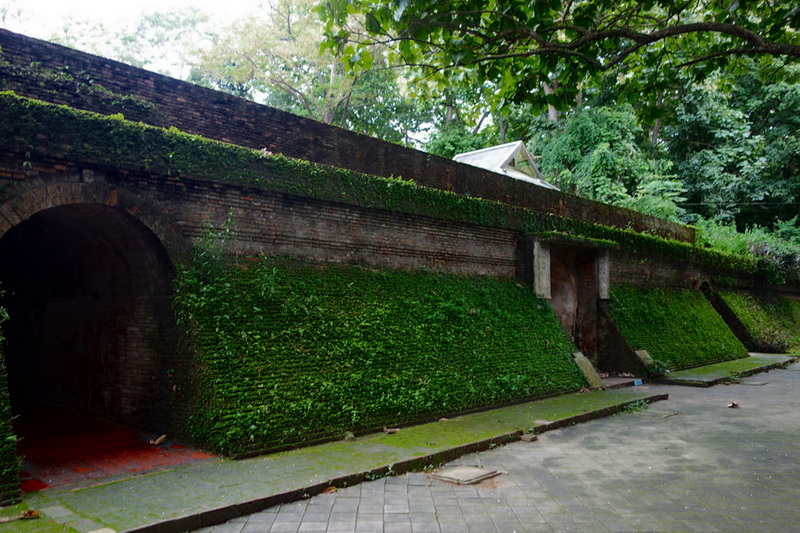 Moss-covered brick bridge with archway and lush trees surrounding it at Umong Temple.