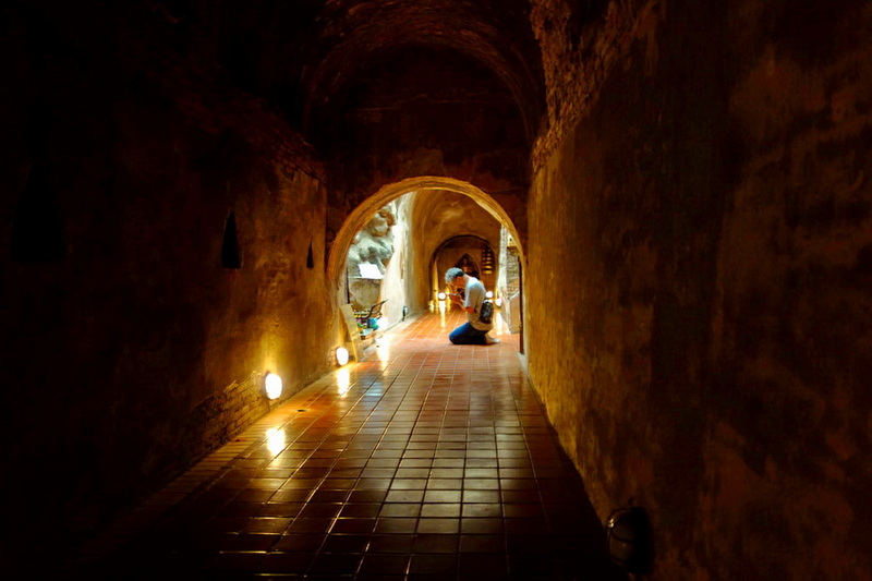 Person kneeling inside a stone tunnel with arched openings and warm lighting at Wat Umong.