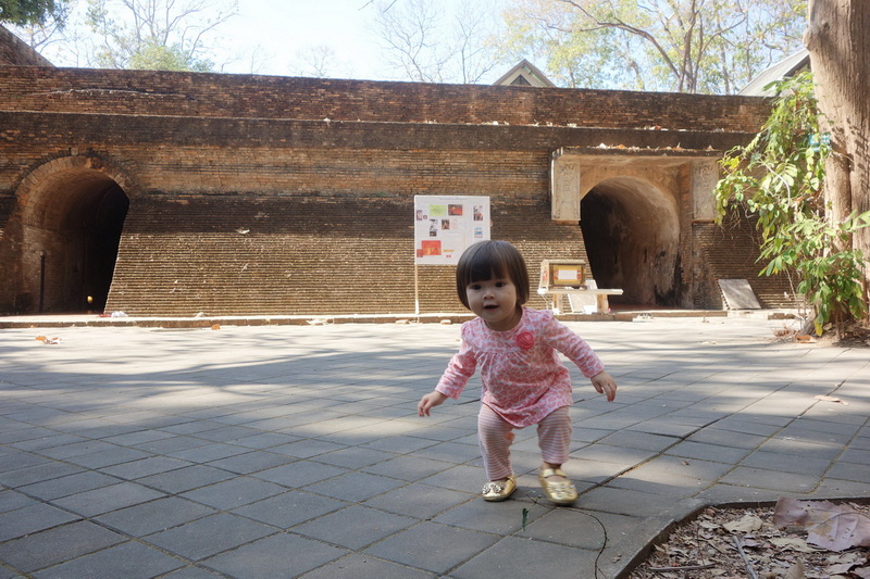 Child at Historic Brick Wall at Wat Umong Young girl in pink standing on a paved area in front of an ancient brick wall with arches at Wat Umong.