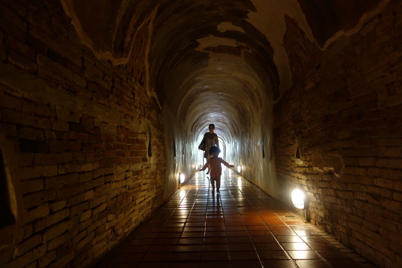 Children walking through a brick tunnel with lights on the floor at Wat Umong.