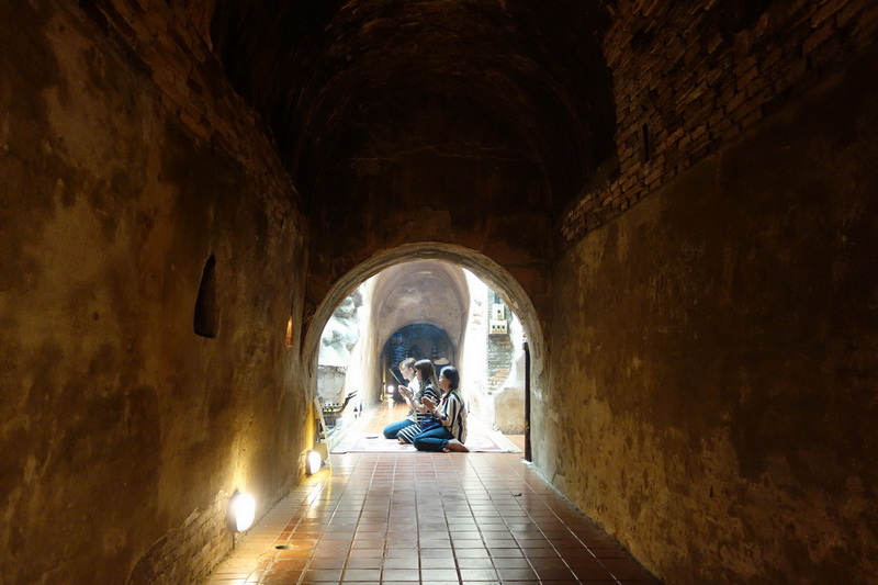 People Praying Inside Tunnel at Umong Temple People praying inside a brick-lined tunnel with soft lighting at the entrance at Umong Temple.