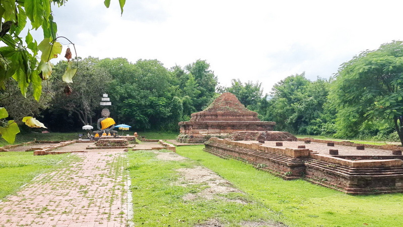 Ancient brick ruins with pathway surrounded by green trees and grass at Wiang Kum Kam.