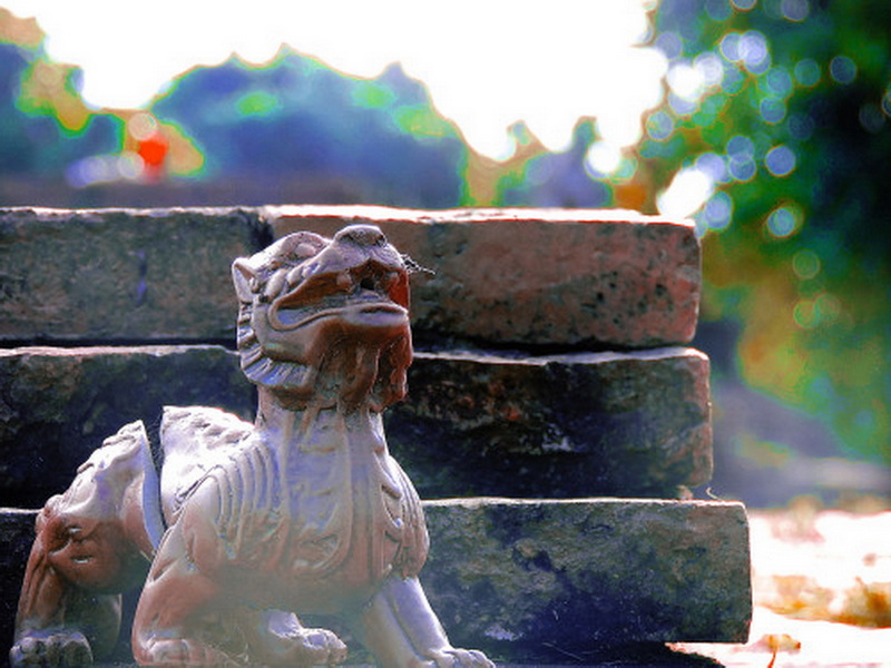 Stone lion statue on brick structure with green foliage in background at Wiang Kum Kam.