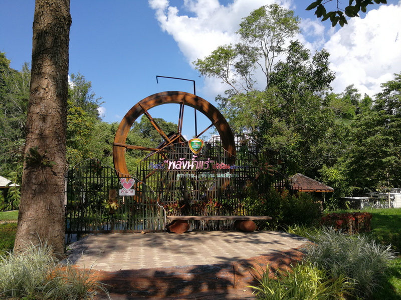 Wooden wheel sculpture with fence and trees in a lush outdoor setting at Chae Son National Park.