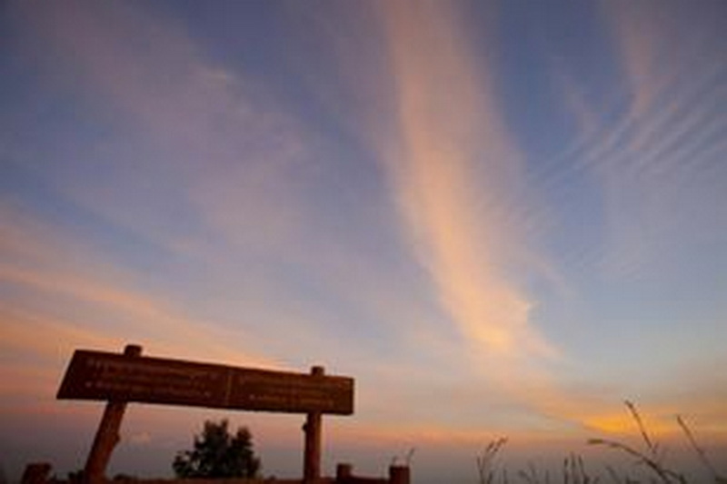 Silhouetted wooden signboard against a vibrant sunset sky with colorful clouds at Doi Khun Tan National Par.