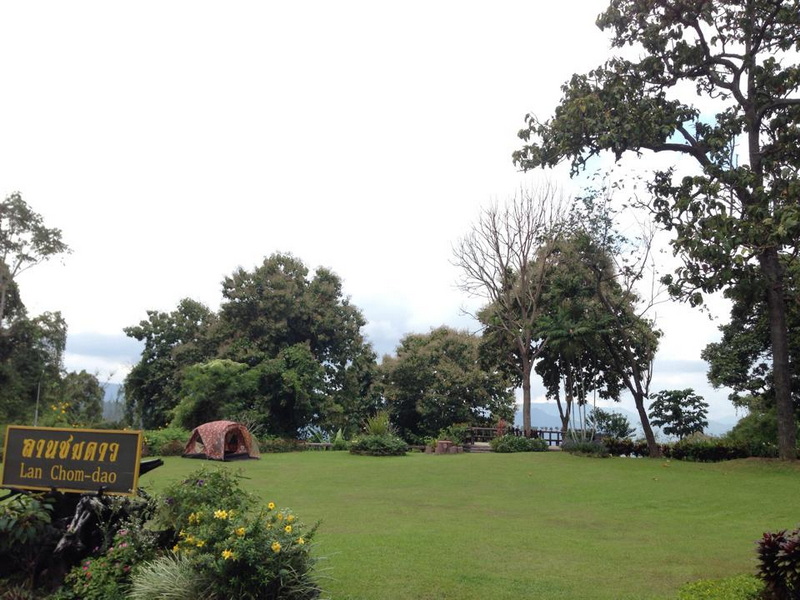Park Scene with Tent and Sign at Doi Khun Tan National Par A green park with trees, a tent, and a sign under cloudy sky at Doi Khun Tan National Par.