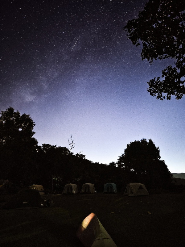 Camping tents under a night sky filled with stars and a meteor streak at Doi Khun Tan National Park.