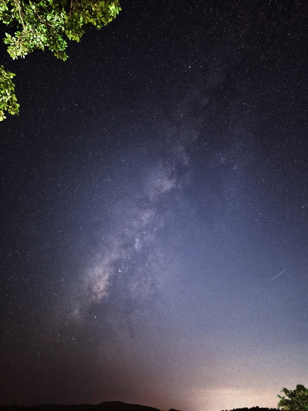 Night sky with stars and the Milky Way above a dark landscape and trees at Doi Khun Tan National Par.