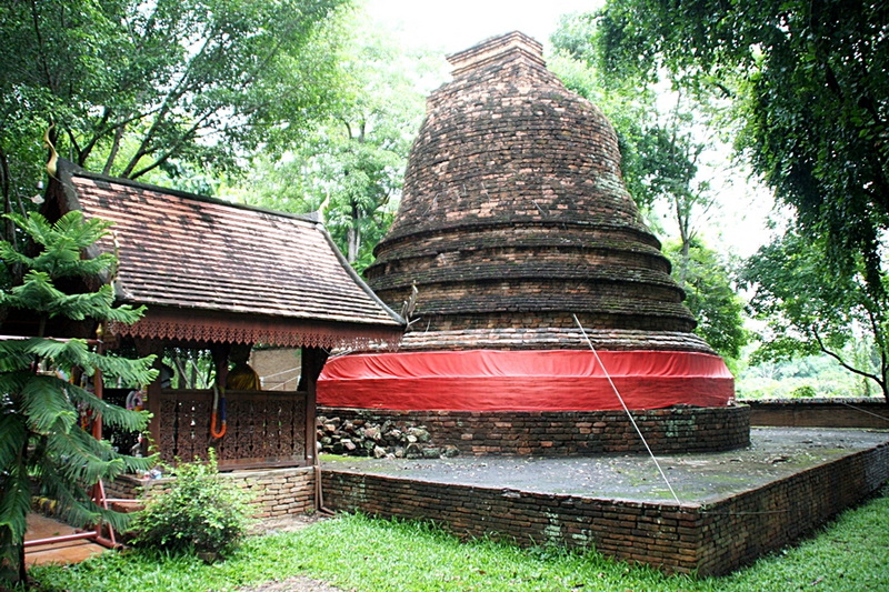 Brick stupa with red cloth surrounded by lush green trees and wooden pavilion at Ku Chang Ku Ma.