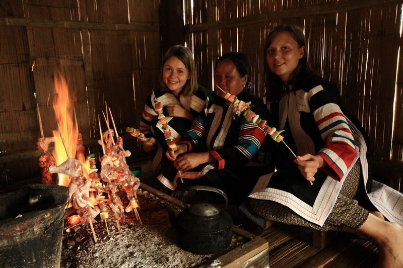 Women cooking skewers over an open fire inside a wooden room at Ban Ja Boe.