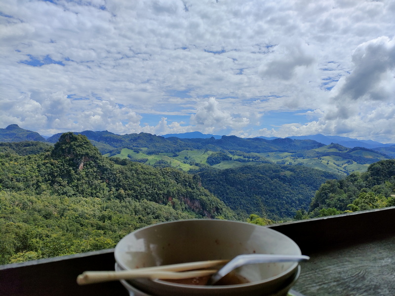 Scenic Hilltop View at Ban Ja Boe Bowl and spoon on a wooden table overlooking green hills and cloudy sky at Ban Ja Boe.