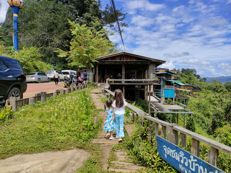 Children Walking Toward Hilltop Structure at Ban Ja Boe Two children walking on a narrow trail heading toward a wooden hilltop structure with parking nearby at Ban Ja Boe.
