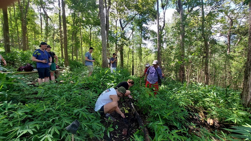 Forest Hiking Adventure at Ban Muang Pam People walking through a lush forest surrounded by tall trees and dense greenery at Ban Muang Pam.