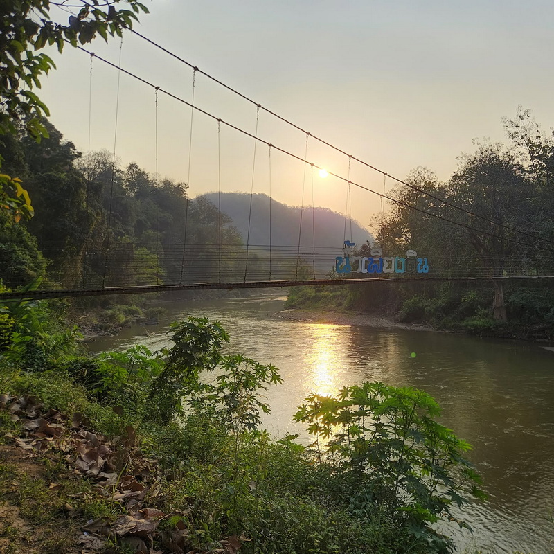 Suspension bridge over a river at sunset with trees and hills in the background at Mae Hong Son.