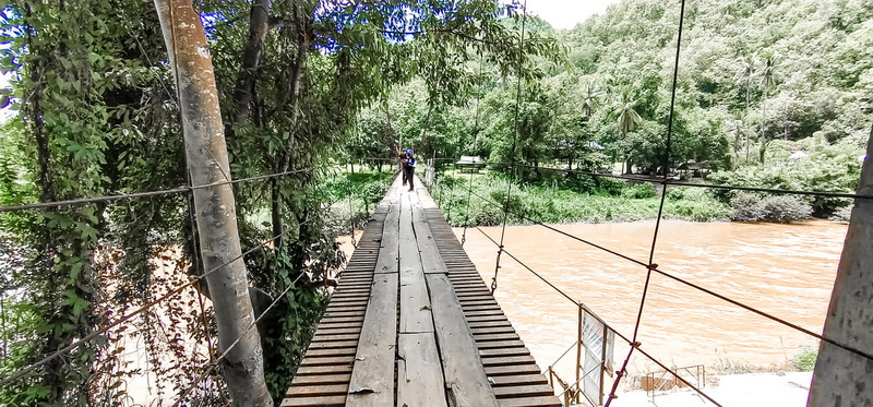 Wooden Suspension Bridge Over River at Ban Nam Phiang Din A suspension bridge over a river with lush green trees on both sides at Ban Nam Phiang Din.