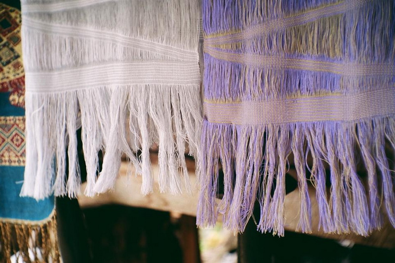 Close-up of vibrant woven textiles with fringes hanging side by side at Ban Nam Phiang Din.