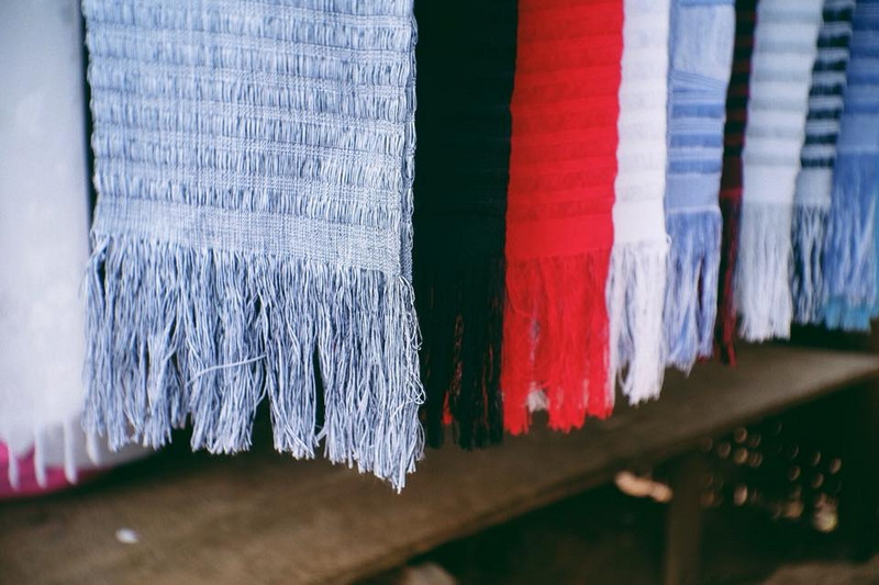 Colorful Woven Fabrics Display at Ban Nam Phiang Din Close-up of colorful woven fabrics hanging on a wooden rack at Ban Nam Phiang Din.
