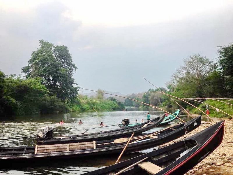 Boats docked along the riverbank with swimmers enjoying the water and surrounding greenery at Ban Nam Phiang Din.