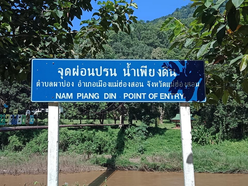 Point of Entry Signboard at Ban Nam Phiang Din Blue signboard with Thai and English text against green trees and mountain background at Ban Nam Phiang Din.