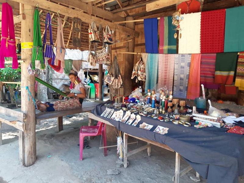 Market Stall with Bags and Textiles at Ban Nam Phiang Din Market stall with hanging bags, textiles, and jewelry in a rustic wooden setting at Ban Nam Phiang Din.