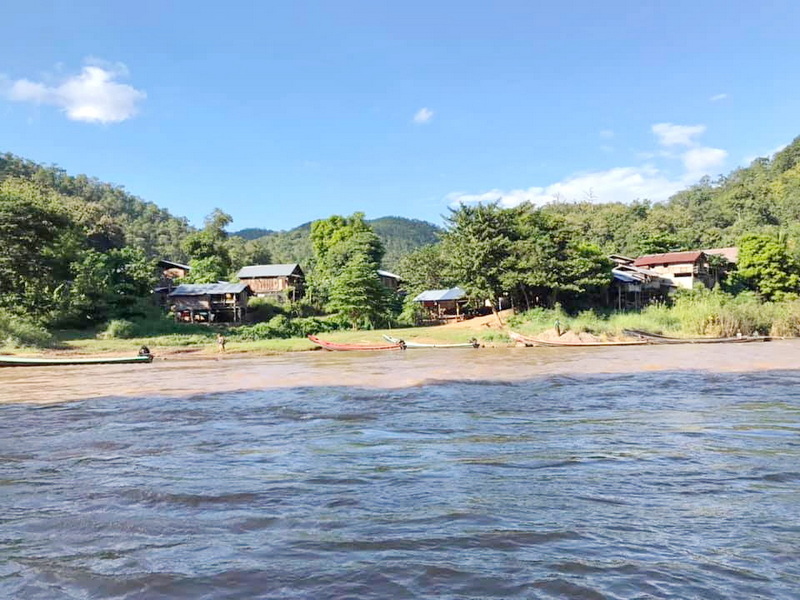 River Scene Near Mae Hong Son River with boats, sandy shoreline, and green hillside under blue sky at Mae Hong Son.