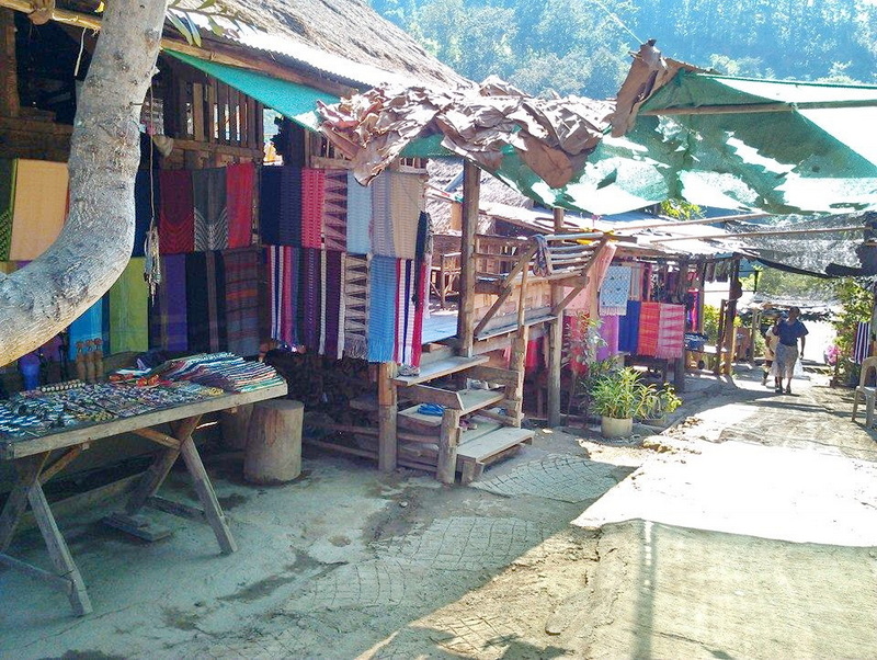 Market stall with colorful fabrics and textiles outside a wooden building with shade cloths at Ban Nam Phiang Din.