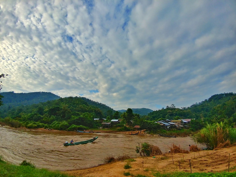 Scenic River Landscape with Hills at Ban Nam Phiang Din River with boats flowing past green hills and small houses under a partly cloudy sky at Ban Nam Phiang Din.