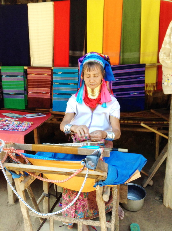 Woman in traditional dress working at a craft stall with vibrant woven fabrics behind her at Ban Nam Phiang Din.