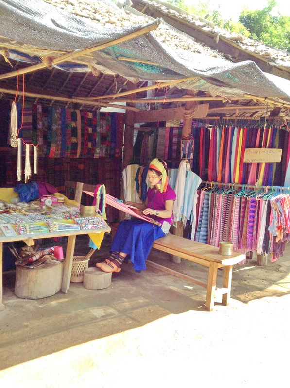 Local Market Textile Shop at Ban Nam Phiang Din Woman sitting in a market stall surrounded by colorful woven textiles and crafts at Ban Nam Phiang Din.