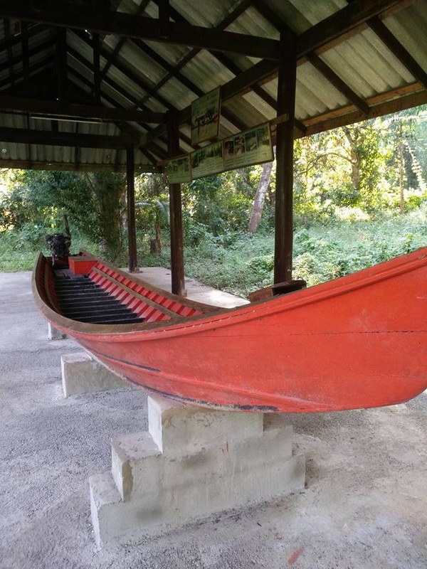 Boat Display at Nature Shelter at Ban Nam Phiang Din Red wooden boat on display under a metal-roofed shelter with info signs and trees behind at Ban Nam Phiang Din.