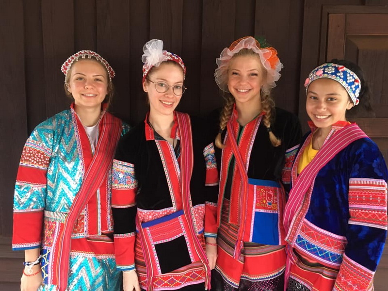 Four women in traditional costumes smiling indoors with wooden background at Ban Pha Mon.