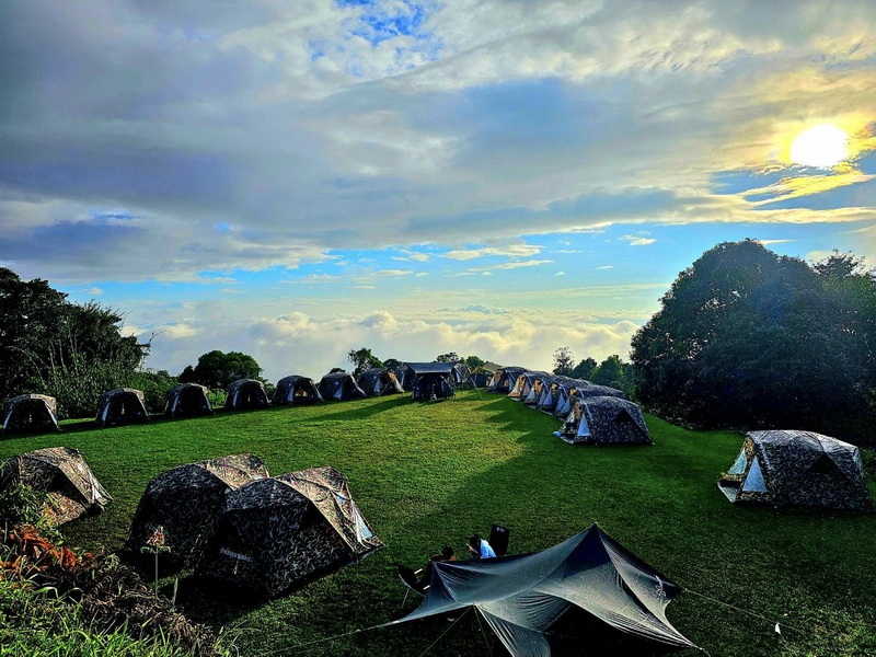 Tents set up on a grassy hilltop with a cloudy sky and sunset in the background at Huai Nam Dang National Park.