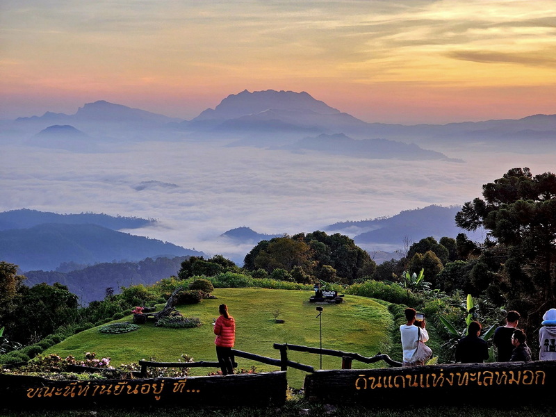 People capturing photos at a viewpoint overlooking mountains and clouds during sunset at Huai Nam Dang National Park.