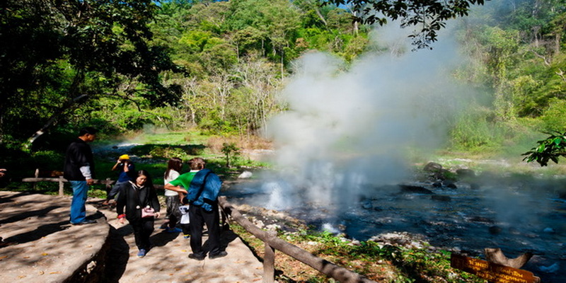 Visitors observe steaming hot springs amidst dense forest scenery at Huai Nam Dang National Park.