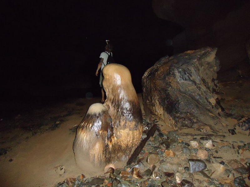 Inside Tham Lod Cave at Mae Lana Cave Person walking inside a dark cave with stalagmites and rocky ground at Mae Lana Cave.